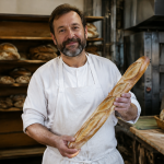 Artisan en tablier blanc tient une baguette croustillante