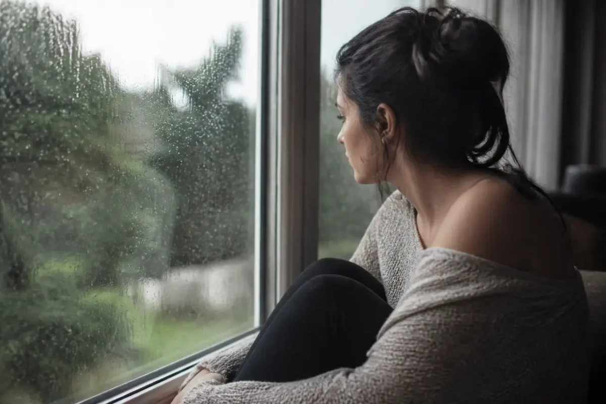 Femme assise seule devant une fenetre pluvieuse